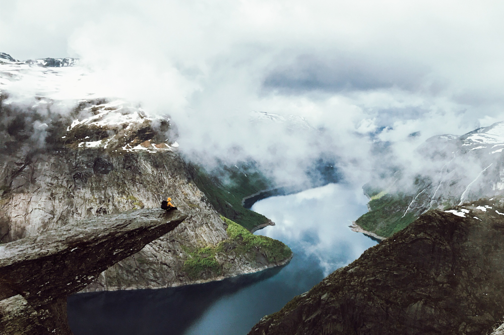 man-sits-end-trolltunga-before-mountains